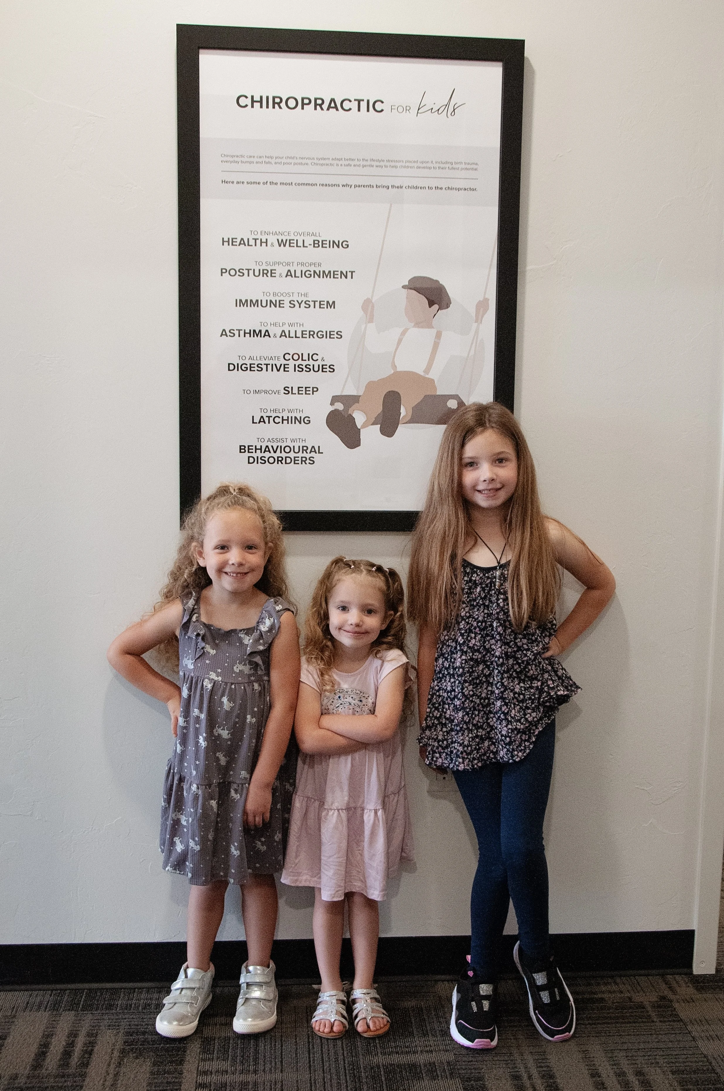 Three smiling kids in front of the pediatric chiropractic sign at REVIVE